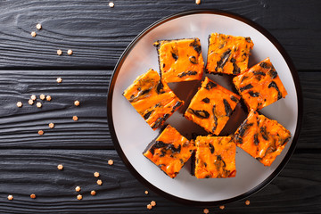 Halloween food dark chocolate brownie topped with a layer of orange cheesecake closeup on the plate. horizontal top view
