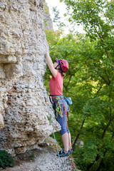 Photo of side view of young athlete woman in red helmet climbing up mountain