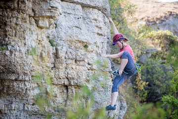 Photo of side view of young athlete woman in red helmet climbing up mountain