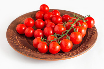 Fresh cherry tomatoes on brown plate isolated on white background