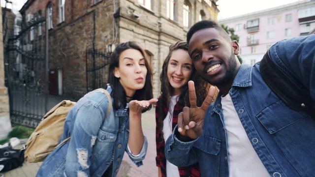 Point of view shot of attractive young men and women travelers taking selfie in the street posing and laughing holding camera. Modern technology and travelling concept.