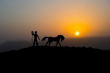 Fototapeta na wymiar Cowboy concept. Silhouette of Cowboys at sunset time. A cowboy silhouette on a mountain with an yellow sky.