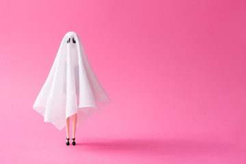 Girl in ghost costume against pastel pink background. Halloween party minimal concept.