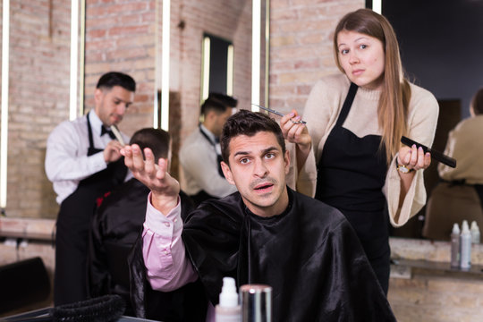 Unpleasantly surprised man with regretting woman hairdresser in salon