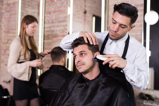 Man barber making hairstyle for male with electric trimmer