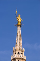 Fototapeta na wymiar Vertical: Rooftop view of golden statue of St Mary, the highest spire on the rooftop of the Duomo di Milano