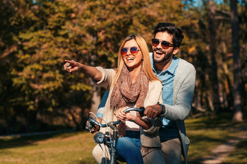 Happy young couple having fun riding a bicycle on sunny day in the park.