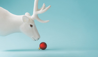 White reindeer with red Christmas bauble decoration on pastel blue background. New Year minimal...