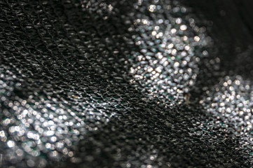 The original texture of the woven network or black nylon net with bokeh and sunlight spots. Black, white, green. Focusing is located on the weave and passes into the soft bokeh.