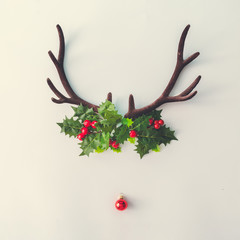 Santas reindeer made of antlers, Holly Christmas plant and red New Year bauble decoration. Minimal...