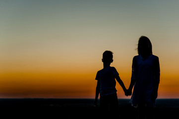silhouette mother and young boy holding hands at sunset. Space for text
