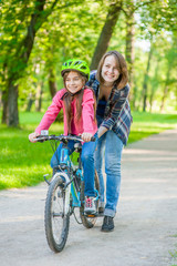 Obraz premium mom teaches her daughter to ride a bicycle in the park