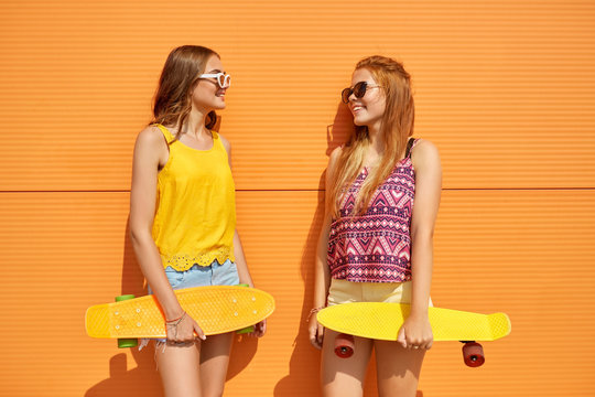 friendship, leisure and people concept - happy teenage girls or friends with short skateboards outdoors in summer