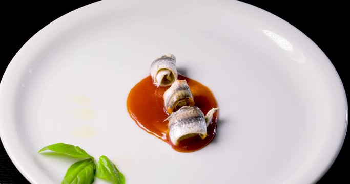 Involtini di Pesce acciughe con miele di arancio, basilico fresco e olio extra vergine di oliva su un piatto da esposizione rotante.