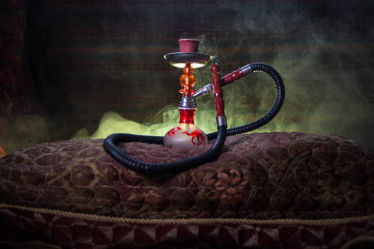 Hookah hot coals on shisha bowl making clouds of steam at Arabian interior. Oriental ornament on the carpet. Stylish oriental shisha in dark with backlight. For Shisha advertisement. Selective focus