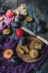 Fresh organic plums and plum slices on wooden board and rustic wooden table, autumn harvest, seasonal fruits, healthy lifestyle, selective focus