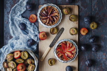 Homemade pie of fresh organic plums on wooden board and rustic table. Seasonal healthy vegeterian food, autumn dessert, top view, selective focus