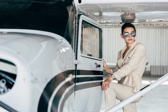 stylish young woman in sunglasses and jacket posing near airplane