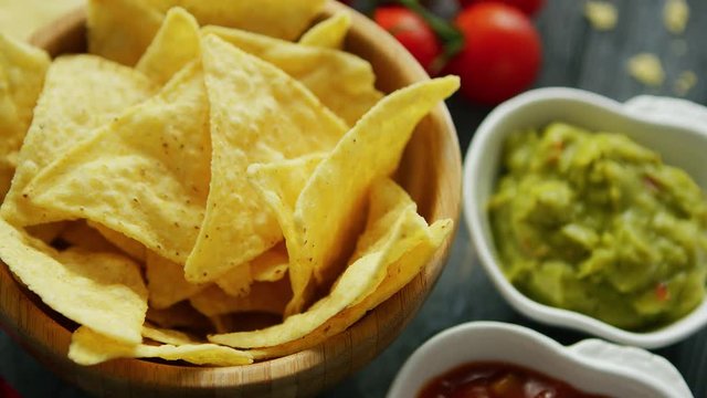 From above closeup shot of wooden bowl with nachos served with salsa and guacamole dip sauces 