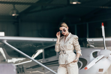 attractive young woman in sunglasses and jacket posing near aircraft