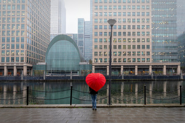 Frau mit herzförmigen Regenschirm steht im Londoner Bezirk Canary Wharf bei herbstlichem Wetter 