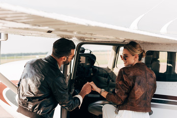 rear view of young man in leather jacket helping girlfriend boarding in airplane