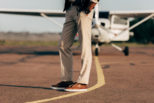cropped image of stylish man in trousers and sneakers near airplane