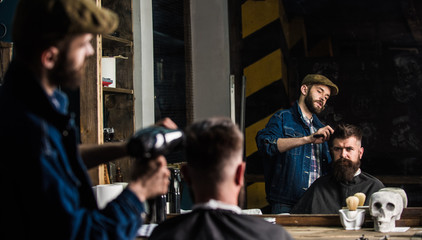 Barber with hairdryer works on hairstyle for bearded man, barbershop background. Styling concept....