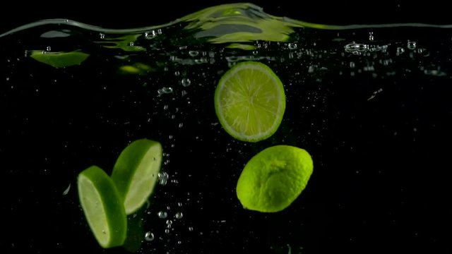 Lime slices fall and float in water, black background, slow motion