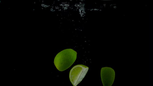 Lime pieces fall and float in water, black background, slow motion