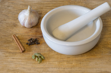 Cardamom, black pepper, cinnamon and garlic lying near mortar on a cutting board