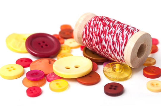 closeup of red and orange buttons and red cotton yarn on white background