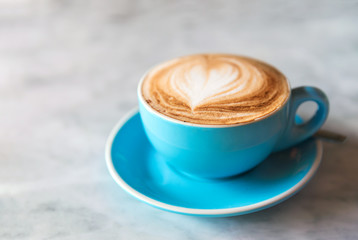 Fresh coffee with heart love foam in blue cup on marble background