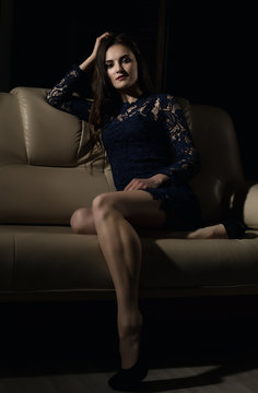 Sensual attractive young woman in a lace dress poses on a sofa.