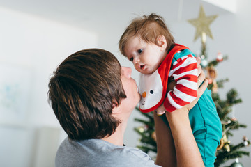 Father holding cute happy baby girl against Christmas tree, family holiday at home