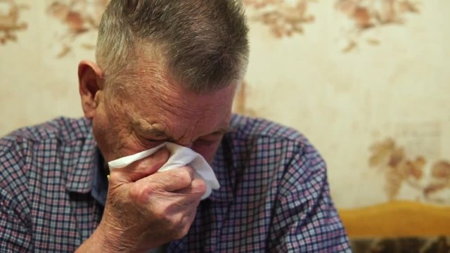 A cold elderly man scribbles snot into a handkerchief and wipes his nose