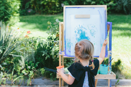 Little cute girl painting on the easel outdoors in the garden