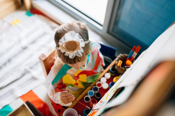Portrait of adorable little girl drawing with paints and palette at easel