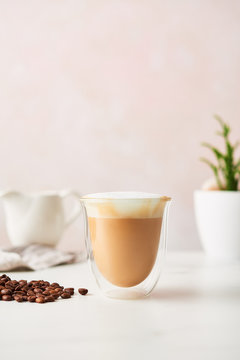 Cappuccino in a double walled glass with roasted coffee beans. Feminine rose background with copy space. High resolution image.