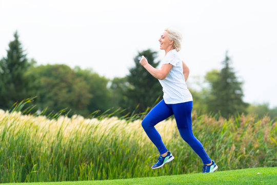 Fit athletic mature woman running alongside reeds