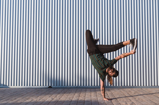 Young man with cap and sports clothes dancing hip hop in the street in a sunny day iron wall background