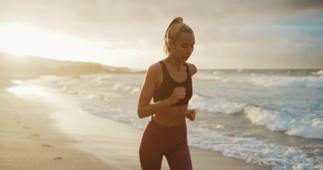 Attractive fitness woman running on the beach at sunset