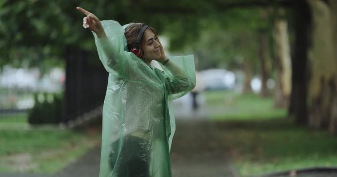 Rain day young woman dacing in the parc and listening music from headphones. 4k