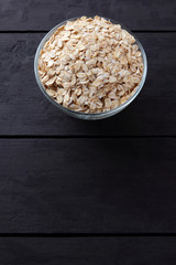 Flakes of oatmeal on wooden boards. Oatmeal on black background. Healthy food for vegans. Preparation of breakfast from natural product. Copy space