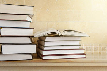 Pile of books with open book on marble shelf. Bookshelf with piled books.