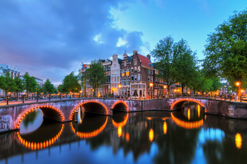 Fototapeta premium Piękny krajobraz słynnych kanałów Amsterdamu w Holandii w nocy z mostami na kanale cesarza (keizersgracht) i kanale Leidse (Leidsegracht)