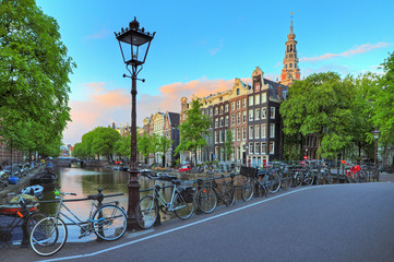 Naklejka premium Pejzaż Amsterdamu o zachodzie słońca z uliczną latarnią przy słynnym kanale Kloveniersburgwal i południowym kościele w Holandii