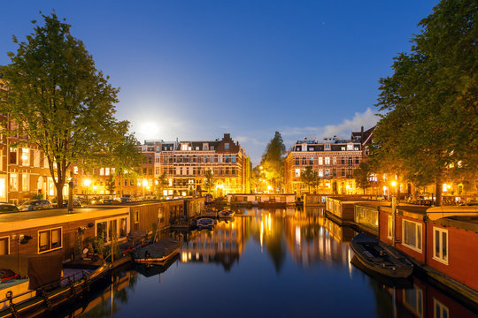 Beautiful cityscape of the famous canals of Amsterdam, the Netherlands, at night with a mirror reflection and houseboats
