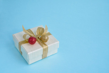 White gift or present box with red-golden Christmas decoration on blue background. Copy space.