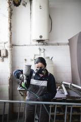 Strong and worthy woman doing hard job. She using industrial spray compressor for painting some metal products.
